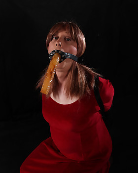 Luci May is dressed in a lucious red dressed and as about to be gagged.